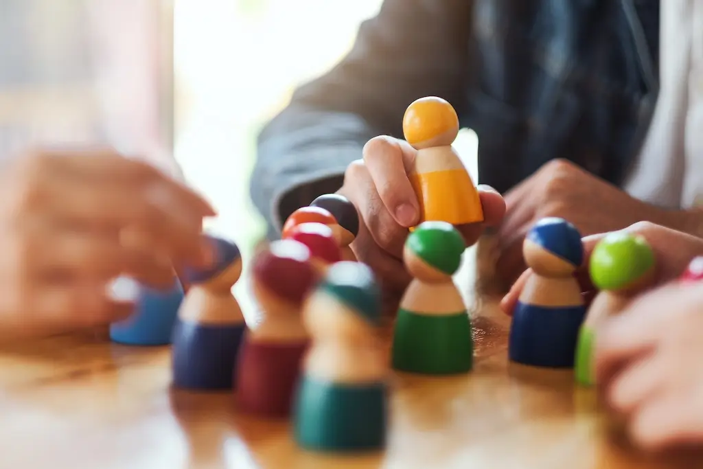 Close-up of hands playing with colourful wooden figures on a table, representing different people and symbolising the diversity and individuality of those on the autism spectrum.