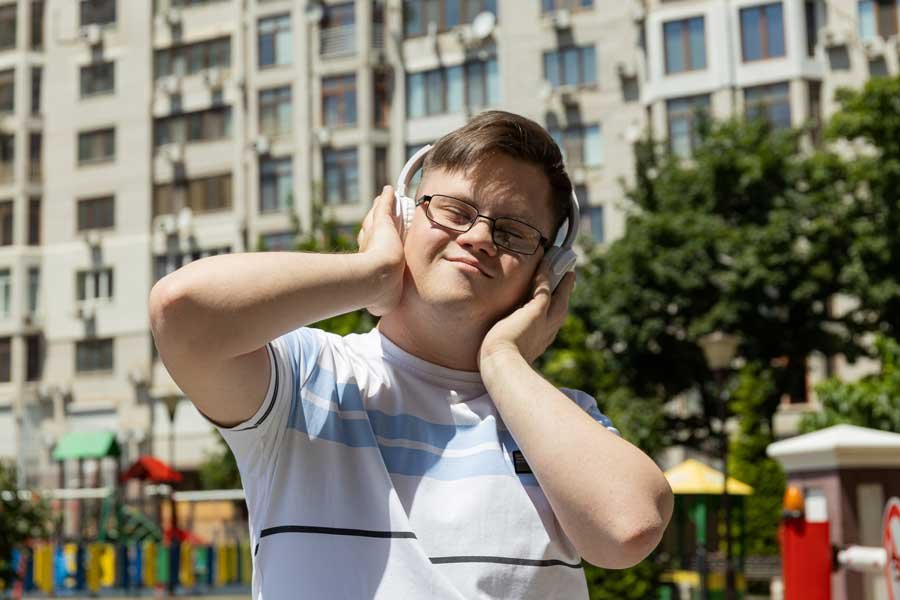 Young man with Down syndrome enjoying music with headphones outside an apartment building, showcasing his confidence and joy through NDIS Supported Independent Living.