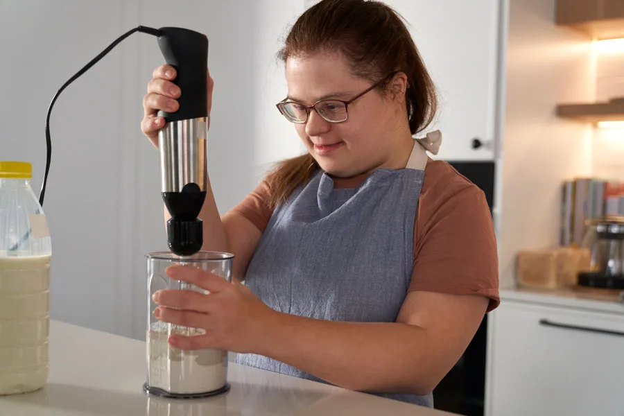 Young woman with Down syndrome using a blender in the kitchen, demonstrating her skills and independence through NDIS support for independent living.