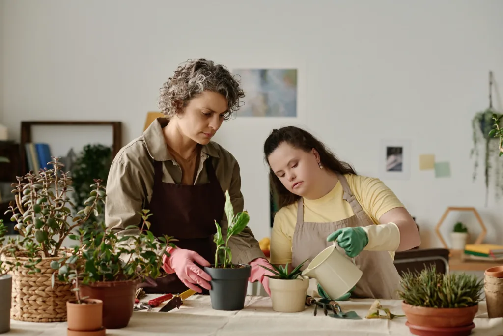 A woman assisting a young girl with Down syndrome in potting plants, illustrating in-home support SIL.