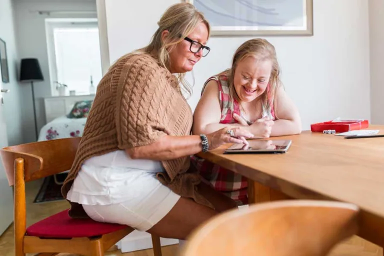 A carer assisting a woman with Down syndrome at a table, highlighting compassionate support and care.