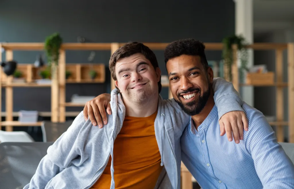 A young man with Down syndrome smiling and embracing his friend, highlighting the theme of community participation.