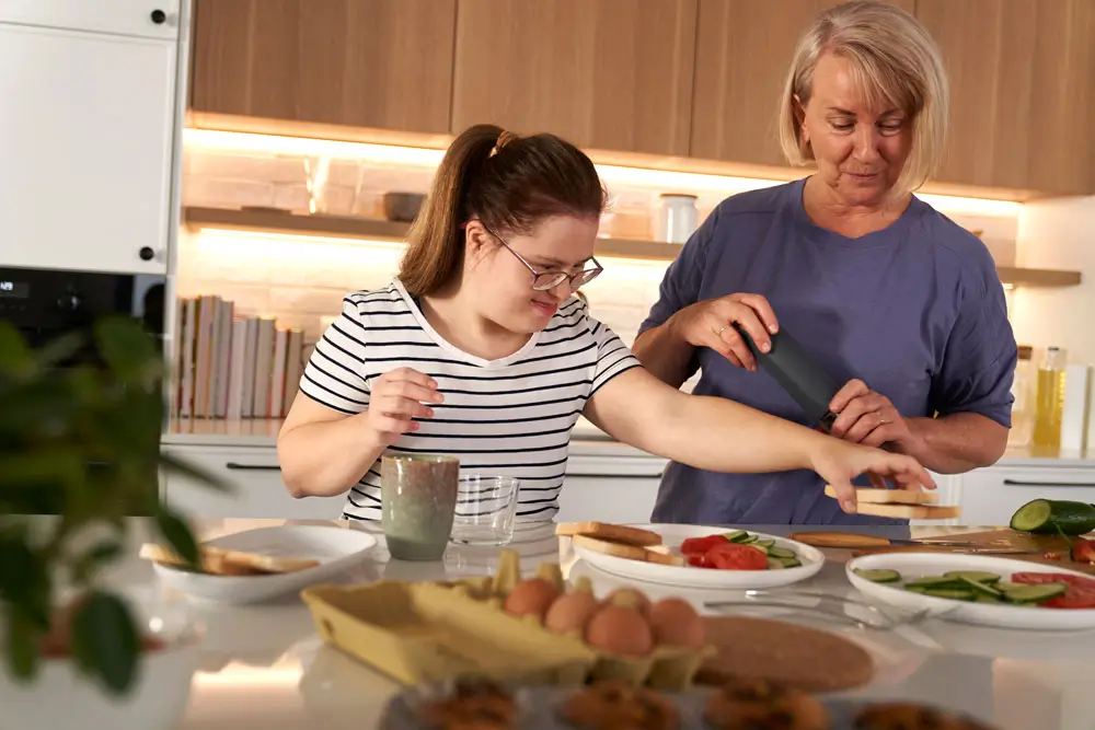 A cooking class where an instructor from NDIS Support Services Melbourne assists a young woman with Down Syndrome in meal preparation.