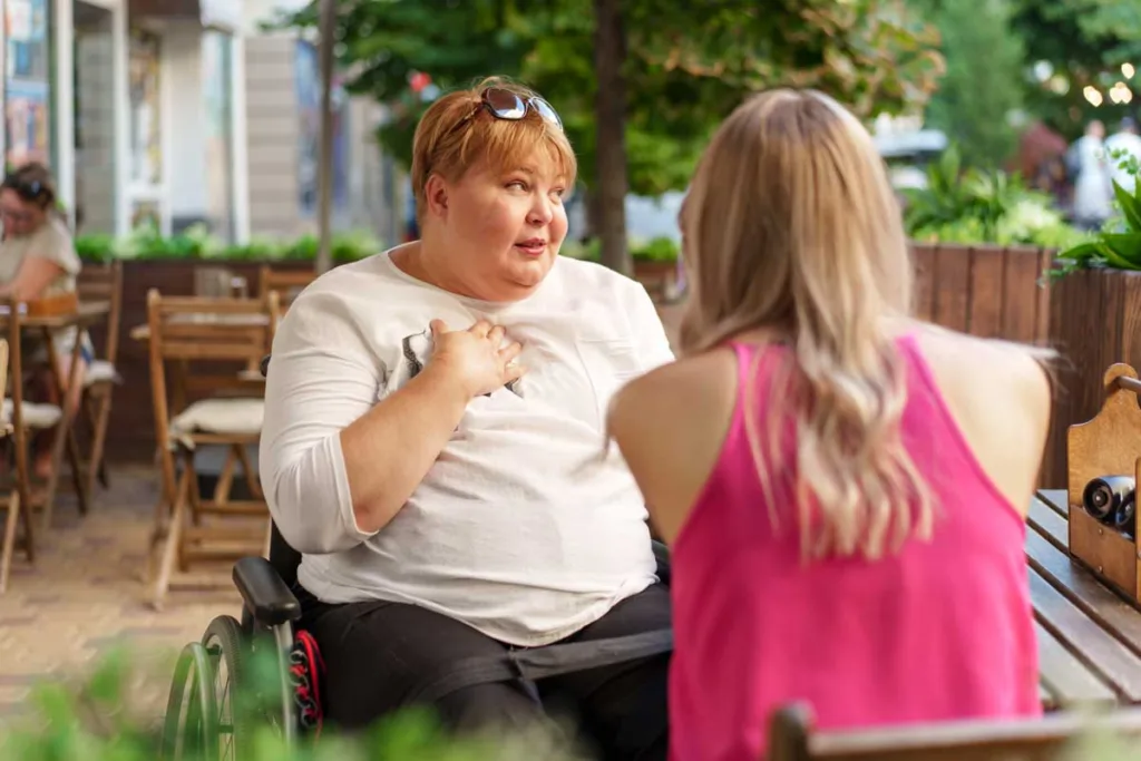 A woman in a wheelchair engaging in a heartfelt conversation about ndis support coordination with a companion at an outdoor café, illustrating accessibility and community connection.