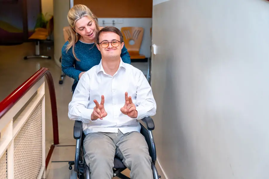 A young man in a wheelchair shows a peace sign with his caregiver, supported by NDIS Support Services Melbourne.