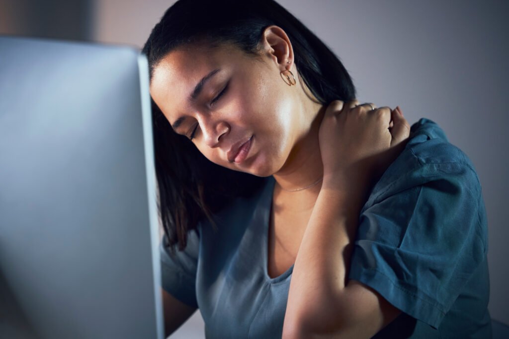 Woman sitting at a desk, holding her neck and looking tired. This image depicts physical fatigue, a common symptom when asking 'What is depression?' and how it affects daily activities.