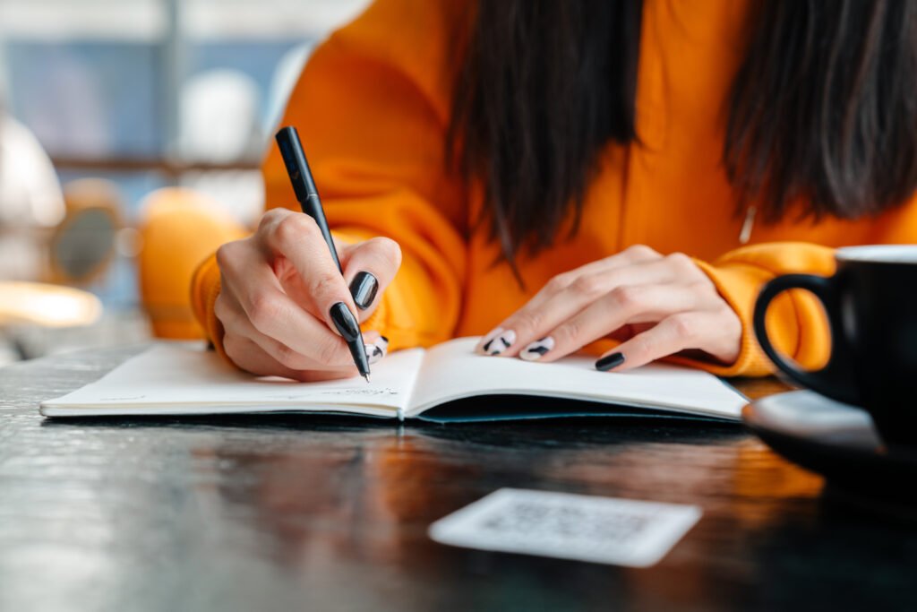 Close-up of a woman writing in a journal at a café. Journalling is often recommended for managing emotions, highlighting how people can understand 'What is depression?’ and cope with it.