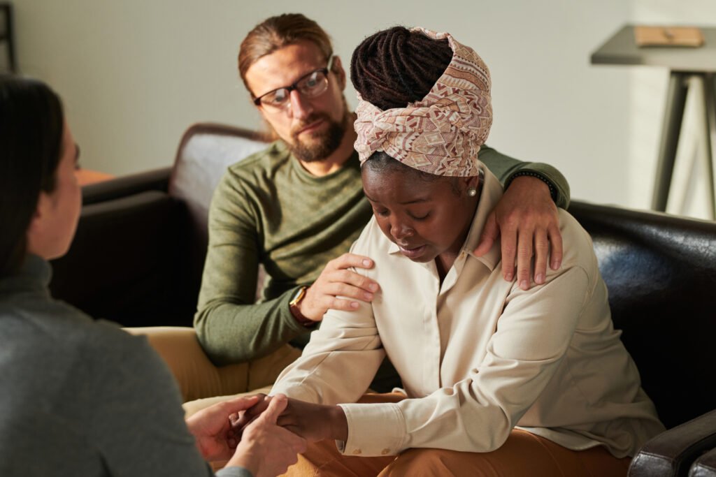 A supportive man with his arm around a distressed woman during a domestic violence counselling session, emphasising care and empathy.