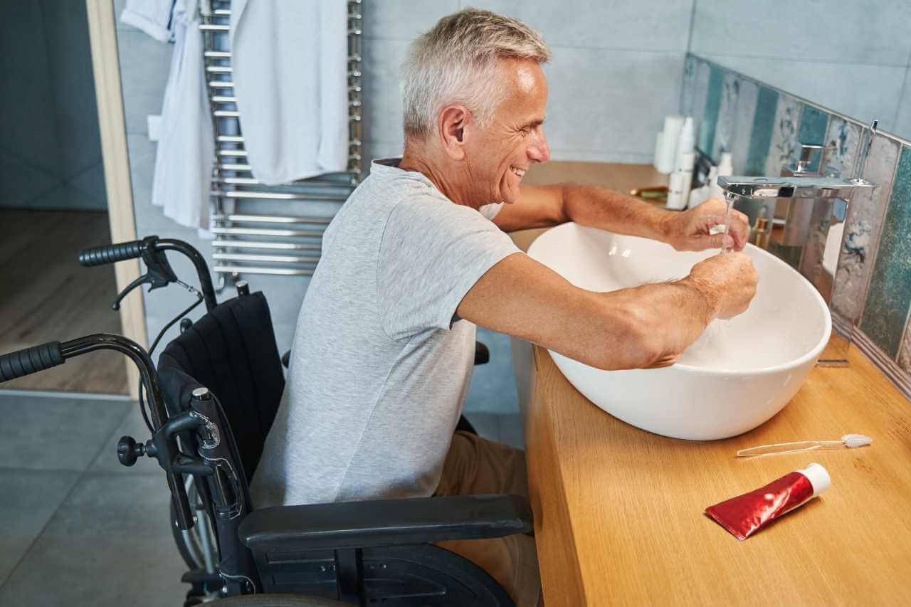 A joyful elderly man in a wheelchair washing his hands in a modern bathroom. This image highlights personal care support in disability services, emphasizing independence and accessibility