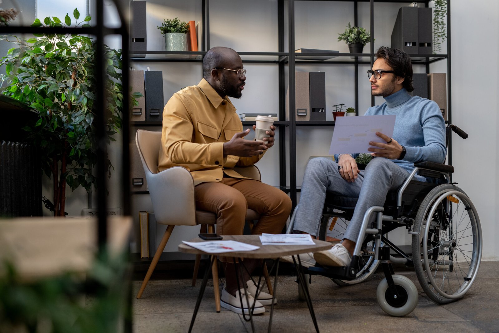 Two men, one in a wheelchair, having a conversation in an office setting, illustrating employment support services for people with disabilities in Australia.