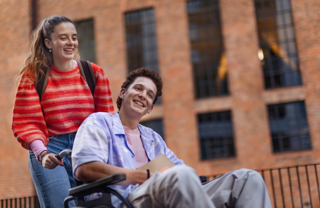 A smiling man in a wheelchair enjoys a day out with a friend, highlighting the positive impact of NDIS service providers on social inclusion.